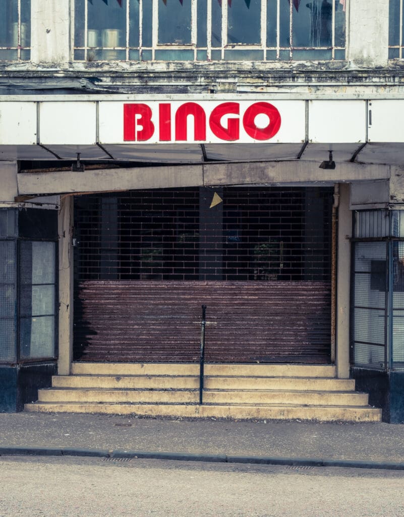 A closed bingo hall with a faded "BINGO" sign above a gated entrance. The steps leading up to the door are worn, and the building appears old and unused.