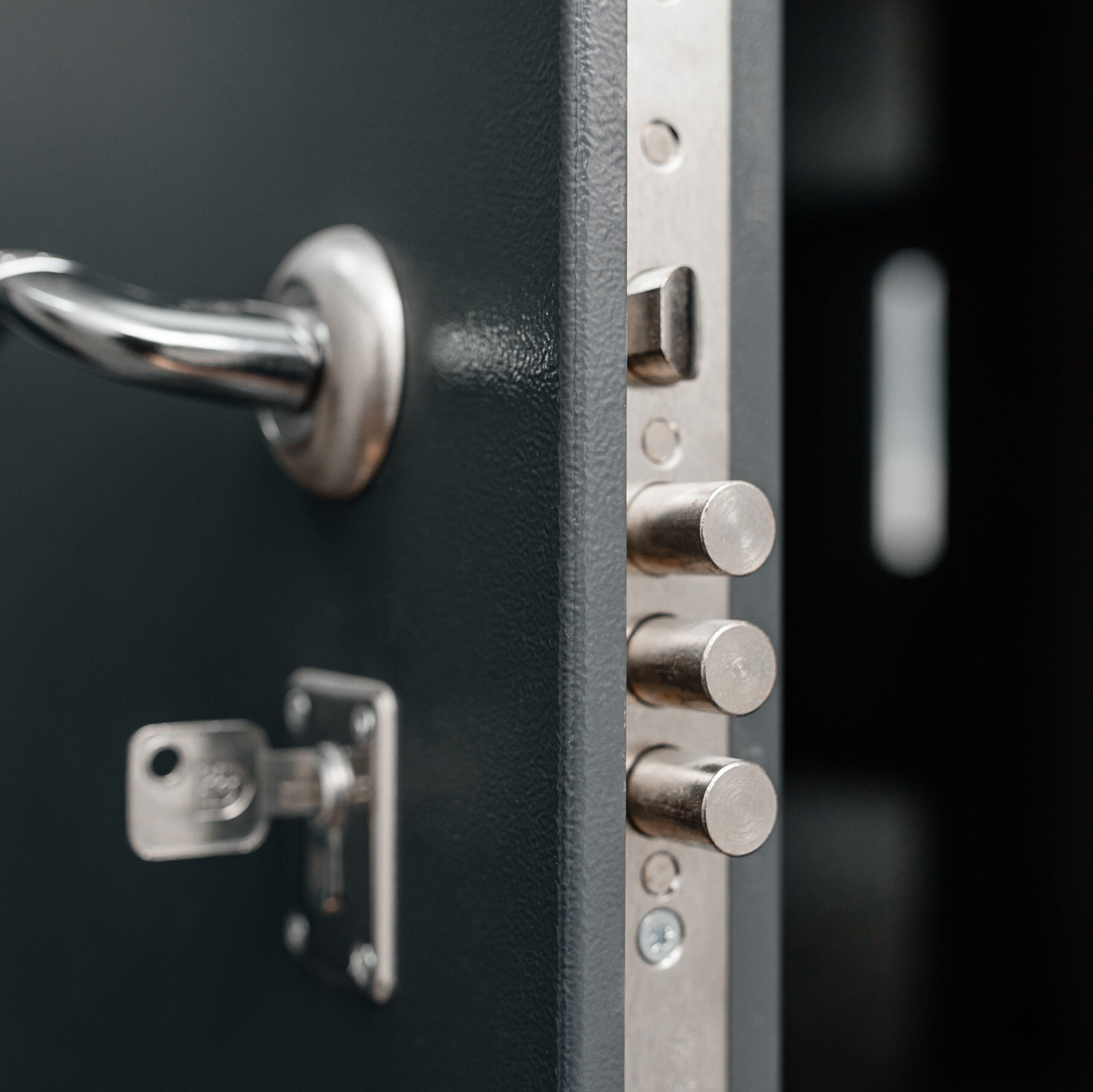 Close-up of a partially open metal door with a secure lock system, showing three cylindrical locking bolts extended and a metallic handle on the left side.